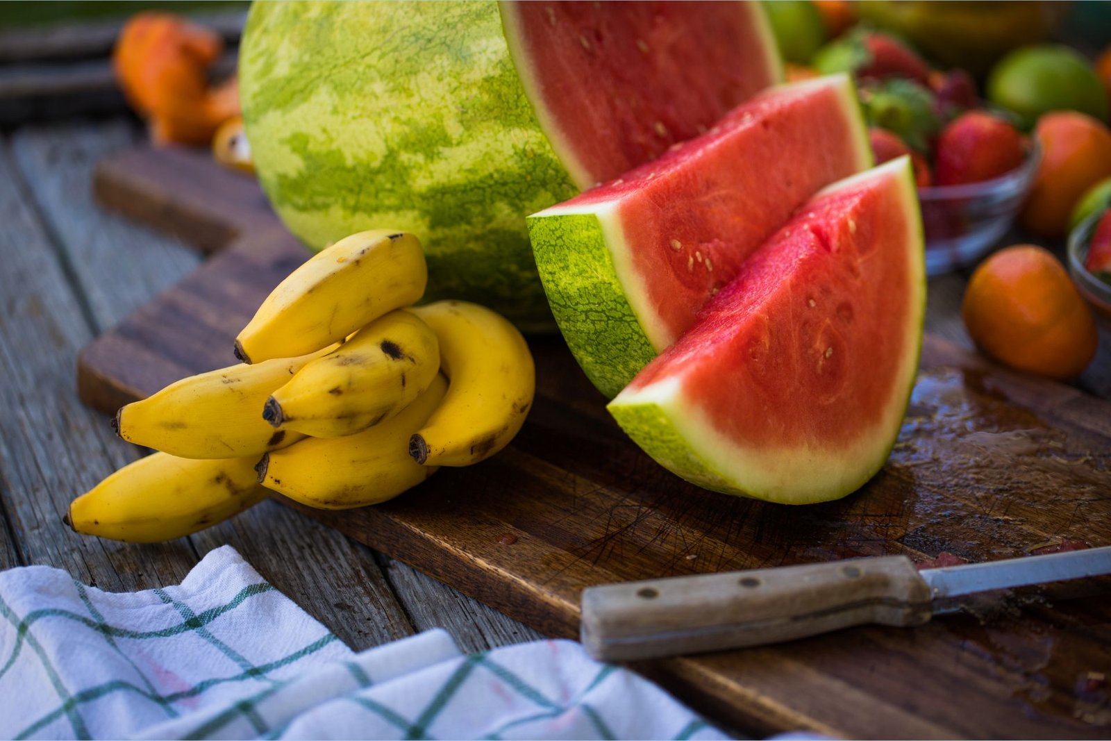 Des bananes riches en potassium sont posées sur une planche à découper à côté d'une pastèque coupée en tranches et riche en L-citrulline.
